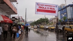 In this photo taken on Monday, July 28, 2014, people hang out in a street under a banner with caution about Ebola, in Monrovia, Liberia. 