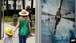 In this June 27, 2020 photo, people walk by a poster promoting the long-awaited Christopher Nolan film "Tenet," in Los Angeles. 