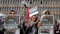 FILE - Women hold copies of Zaman newspaper, headlined 'Black Day of Democracy,' to protest the detention of its editor and other journalists in raids by the Turkish government in Ankara.