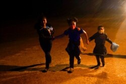 FILE - Three young migrants hold hands as they run in the rain at an intake area after turning themselves in upon crossing the U.S.-Mexico border, May 11, 2021, in Roma, Texas.