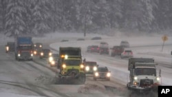 Washington Dept. of Transportation snow plows work on a stretch of eastbound Interstate Highway 90, Dec. 9, 2021, as snow falls near Snoqualmie Pass in Washington state.