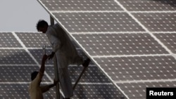 FILE - Technicians work on a solar panel about 25 km (15 miles) from Karachi, Pakistan, June 18, 2010. 