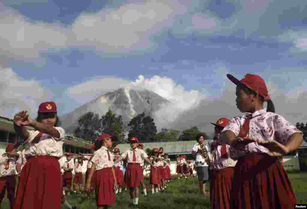 Murid-murid Sekolah Dasar melakukan senam pagi di desa Berastepu, dengan latar belakang Gunung Sinabung yang meletus di di kabupaten Karo, Sumatera Utara (7/11). (Reuters/Tarmizy Harva)