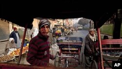 Indian rickshaw drivers wait for passengers as vendors sell fruit and vegetables at a street market in New Delhi, India, December 15, 2011.
