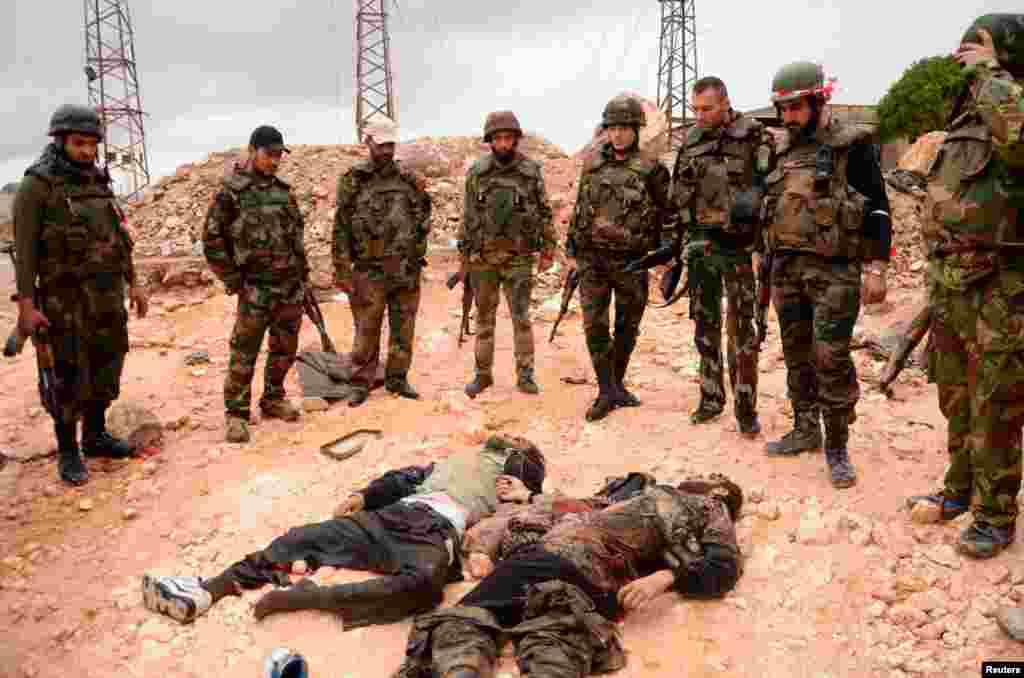 Forces loyal to Syria's President Bashar al-Assad stand near the dead bodies of two members of the Free Syrian Army at the Shikh Saad neighborhood, in Aleppo, November 11, 2012. 