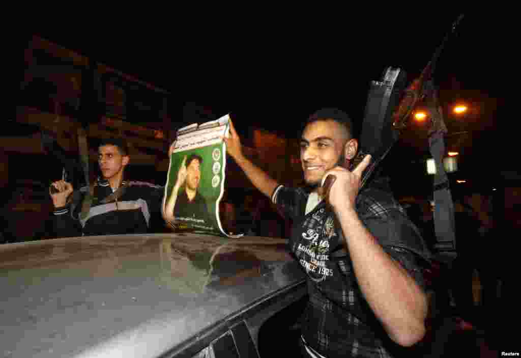 After eight days of conflict Palestinian gunmen hold aloft an image of Hamas military chief Ahmed Jaabari, who was killed by an Israeli air strike, Gaza City, Nov. 21, 2012.