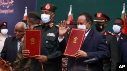 In this photo provided by the Sudan Transitional Sovereign Council, Sudan's top general Abdel Fattah Al-Burhan, center left, and Prime Minister Abdalla Hamdok hold documents during a ceremony to reinstate Hamdok.