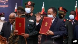 In this photo provided by the Sudan Transitional Sovereign Council, Sudan's top general Abdel Fattah Al-Burhan, center left, and Prime Minister Abdalla Hamdok hold documents during a ceremony to reinstate Hamdok.