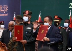 In this photo provided by the Sudan Transitional Sovereign Council, Sudan's top general Abdel Fattah Al-Burhan, center left, and Prime Minister Abdalla Hamdok hold documents during a ceremony to reinstate Hamdok.