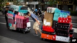 FILE - Workers pull carts loaded with shoes made by Nike and other Chinese and foreign shoe manufacturers along a street in Beijing.