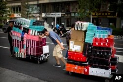 FILE - Workers pull carts loaded with shoes made by Nike and other Chinese and foreign shoe manufacturers along a street in Beijing, China, Aug. 10, 2018.