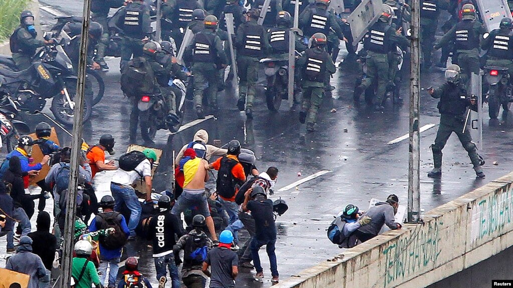 En esta foto de archivo se ve a un miembro de las fuerzas anti disturbios (derecha) apunta lo que parece ser una pistola hacia una multitud de manifestantes durante una protesta contra el gobierno del presidente venezolano, Nicolás Maduro, en Caracas, el 19 de junio de 2017.