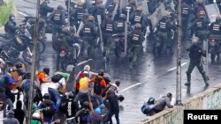 Un miembro de las fuerzas de seguridad de Venezuela (derecha) apunta lo que parece ser una pistola hacia una multitud de manifestantes durante una protesta contra el gobierno del presidente Nicolás Maduro en Caracas, el 19 de junio de 2017.