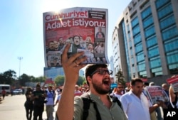 FILE - Activists, one holding a recent copy of the Cumhuriyet newspaper, march in Istanbul, July 24, 2017, protesting against a trial of journalists and staff from the newspaper, accused of aiding terror organizations.