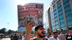 FILE - Activists, one holding a recent copy of the Cumhuriyet newspaper, march in Istanbul, July 24, 2017, protesting against a trial of journalists and staff from the newspaper, accused of aiding terror organizations. 