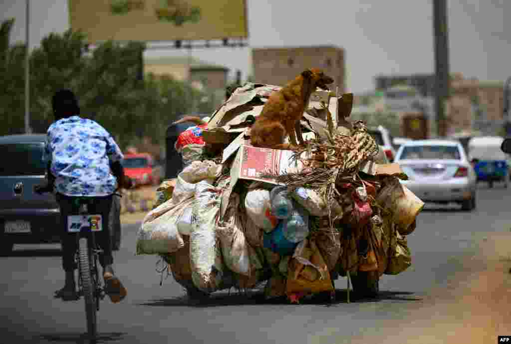 A boy rides his bicycle past a vehicle transporting domestic garbage, in the capital Khartoum, Sudan.