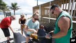 Kristen Allen (tengah, depan) dan Travis Scott (kanan) bersiap menghadapi badai Matthew dengan mengisi tas dengan pasir untuk mengantisipasi banjir agar tidak masuk ke toko suvenir di Cocoa Beach, Florida, 5 Oktober 2016. (AP Photo/John Raoux)