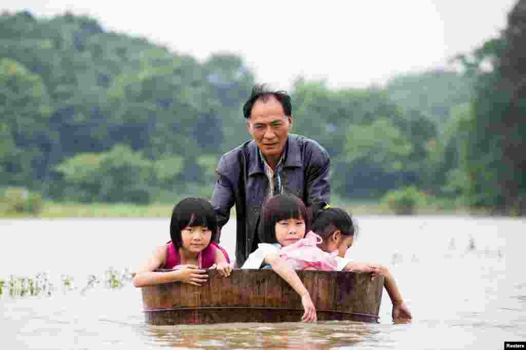 Seorang ayah mendorong tong dari kayu sebagai perahu bagi anak-anaknya saat banjir melanda Duchang, Jiangxi, China.
