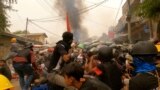 Protesters use slingshots while taking cover behind a barricade as smoke rises from burning debris during ongoing protests against the military coup, in Monywa, Sagaing region, Myanmar March 29, 2021 in this still image from video obtained by REUTERS AT