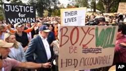 Australian Prime Minister Anthony Albanese, wearing a hat and standing next to a sign in front, attends a rally to a call for action to end violence against women, in Canberra, April 28, 2024.