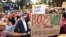 Australian Prime Minister Anthony Albanese, wearing a hat and standing next to a sign in front, attends a rally to a call for action to end violence against women, in Canberra, April 28, 2024.
