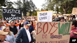 Perdana Menteri Australia Anthony Albanese (mengenakan topi dan berdiri di samping poster) menghadiri aksi demo, yang menyerukan penghentian kekerasan terhadap perempuan, di Canberra, pada 28 April 2024. (Foto: Lukas Coch/AAP Image via AP)