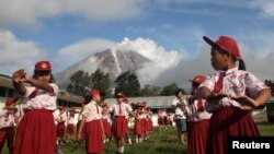 Murid-murid sekolah di desa Berastepu, Karo, melakukan senam pagi dengan latar belakang Gunung Sinabung yang mengeluarkan abu (7/11). (Reuters/Tarmizy Harva)