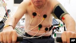 FILE - A man sits on an ergometer during an electrocardiogram in a doctor's surgical office.