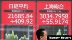 A man walks past an electric screen showing Japan's Nikkei and Shanghai Stock Exchange markets' indices outside a brokerage in Tokyo, July 1, 2019.