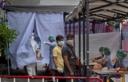 Muaythai boxing fighters and officials gather at a makeshift screening facility as a man in a Hazmat suite talks with a nurse outside Rajadamnern boxing stadium in Bangkok, Thailand, Thursday, March 19, 2020.