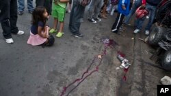 Seorang anak perempuan menutup matanya saat duduk di lokasi pembunuhan di Tegucigalpa, Honduras (1/12). (AP/Esteban Felix)