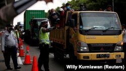 Seorang polisi mengenakan masker mengatur lalu lintas di sebuah pos pemeriksaan jalan raya di Bekasi, 24 April 2020.