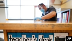 FILE - Des Moines Public Schools custodian Joel Cruz cleans a teacher's desk in a classroom at Brubaker Elementary School in Des Moines, Iowa, July 8, 2020.