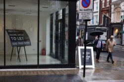 Men wearing protective masks walk past a shutdown store, amid the outbreak of the coronavirus, in London, Britain, Oct. 13, 2020.