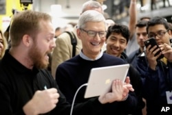 FILE- In this March 27, 2018, file photo Apple CEO Tim Cook smiles as he watches a demonstration on an iPad at an Apple educational event at Lane Technical College Prep High School in Chicago. (AP Photo/Charles Rex Arbogast, File)