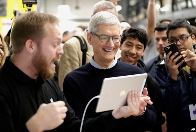 FILE- In this March 27, 2018, file photo Apple CEO Tim Cook smiles as he watches a demonstration on an iPad at an Apple educational event at Lane Technical College Prep High School in Chicago. (AP Photo/Charles Rex Arbogast, File)