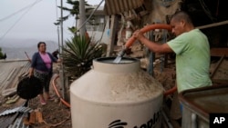 Alfonso Tapullima, right, fills the water tank near his wife Justina Flores, at the Pamplona Alta hilltop neighborhood in Lima, Peru, Friday, March 8, 2024. (AP Photo/Martin Mejia)