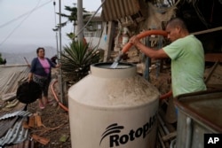 FILE—Alfonso Tapullima, right, fills the water tank at the Pamplona Alta hilltop neighborhood in Lima, Peru, March 8, 2024.