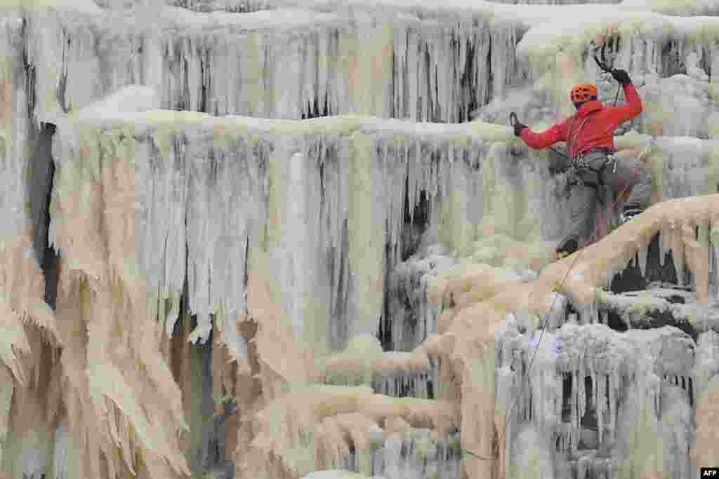 An ice climber ascends Kinder Downfall, a frozen waterfall in the Peak District National Park, near Hayfield, northwest England, as snow blankets the region.