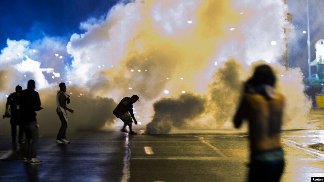 Seorang demonstran jongkok untuk mengambil gas air mata untuk dilemparkan kembali ke polisi yang mengosongkan jalanan setelah pemberlakuan jam malamdi Ferguson, Missouri, 17 Agustus 2014. 