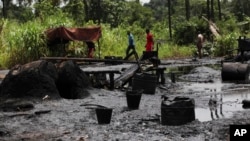 FILE- Men walk past an abandoned illegal refinery in Bayelsa, Nigeria, May 18, 2013. Nigerian authorities in Rivers State unveiled on Friday six military-grade gunboats to help security battle the piracy and oil theft that have plagued the Niger Delta region for decades.