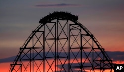 People ride a roller coaster at dusk at Worlds of Fun amusement park Monday, July 3, 2017, in Kansas City, Mo. (AP Photo/Charlie Riedel)