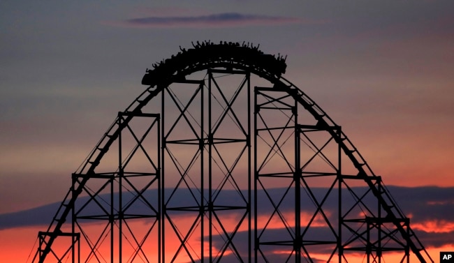 People ride a roller coaster at dusk at Worlds of Fun amusement park Monday, July 3, 2017, in Kansas City, Mo. (AP Photo/Charlie Riedel)