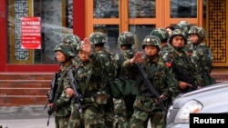 FILE - Paramilitary policemen gesture to stop a photographer from taking pictures as they stand guard after an explosives attack it downtown Urumqi in the Xinjiang Uighur Autonomous Region, May 23, 2014. 