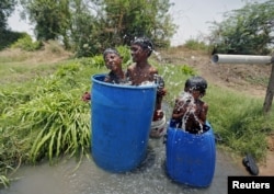FILE - Children sit in plastic containers filled with water as they cool themselves next to a borewell at a farm on a hot summer day on the outskirts of Ahmedabad, India, May 28, 2015.