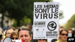 A woman wearing a yellow vest and speaking in a loud hailer, holds a placard reading "Media are the virus ..." during a demonstration against the mandatory COVID-19 health pass in Paris on Sept. 4, 2021