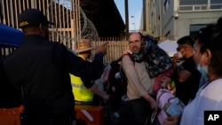 Refugiados ucranianos falam com um funcionário da Alfândega e da Patrulha de Fronteiras dos Estados Unidos enquanto se preparam para atravessar a fronteira, segunda-feira, 4 de abril de 2022, em Tijuana, México.