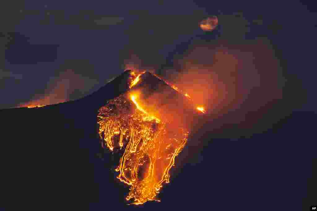 The moon is partially seen in the sky as lava flows from the Mt Etna volcano, near Catania in Sicily, southern Italy.