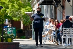 FILE - A member of the wait staff delivers food to outdoor diners along the sidewalk at the Mediterranean Deli restaurant in Chapel Hill, N.C., Apr. 16, 2021.