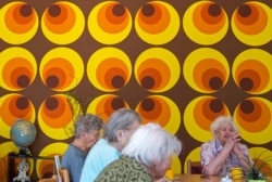 FILE - Residents sit in front of a colorful wallpaper of the 70s in the Alexa Seniors' Residence in Dresden, eastern Germany, May 17, 2017.